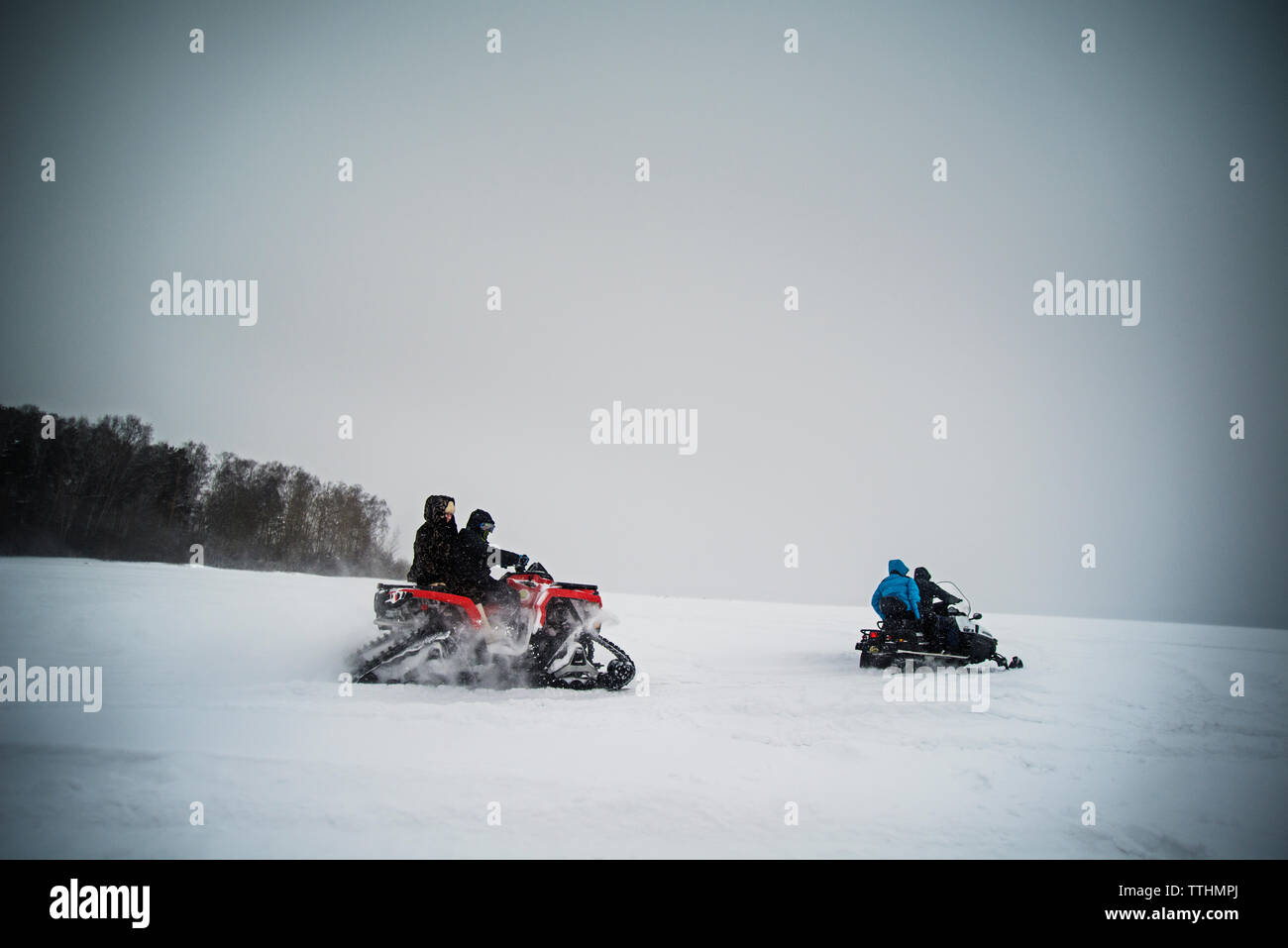 Friends riding snowmobile on field against sky Stock Photo