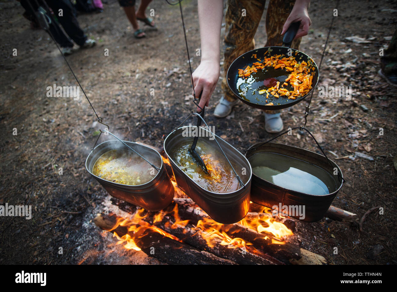 Low section of person preparing food in utensils over bonfire at campsite Stock Photo