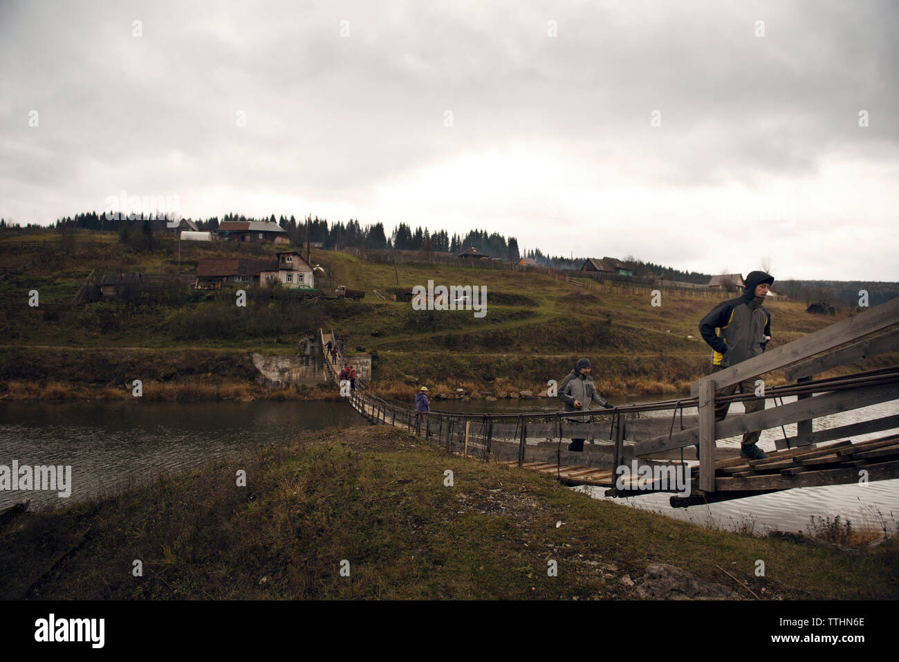 Hikers walking on footbridge over lake against cloudy sky Stock Photo