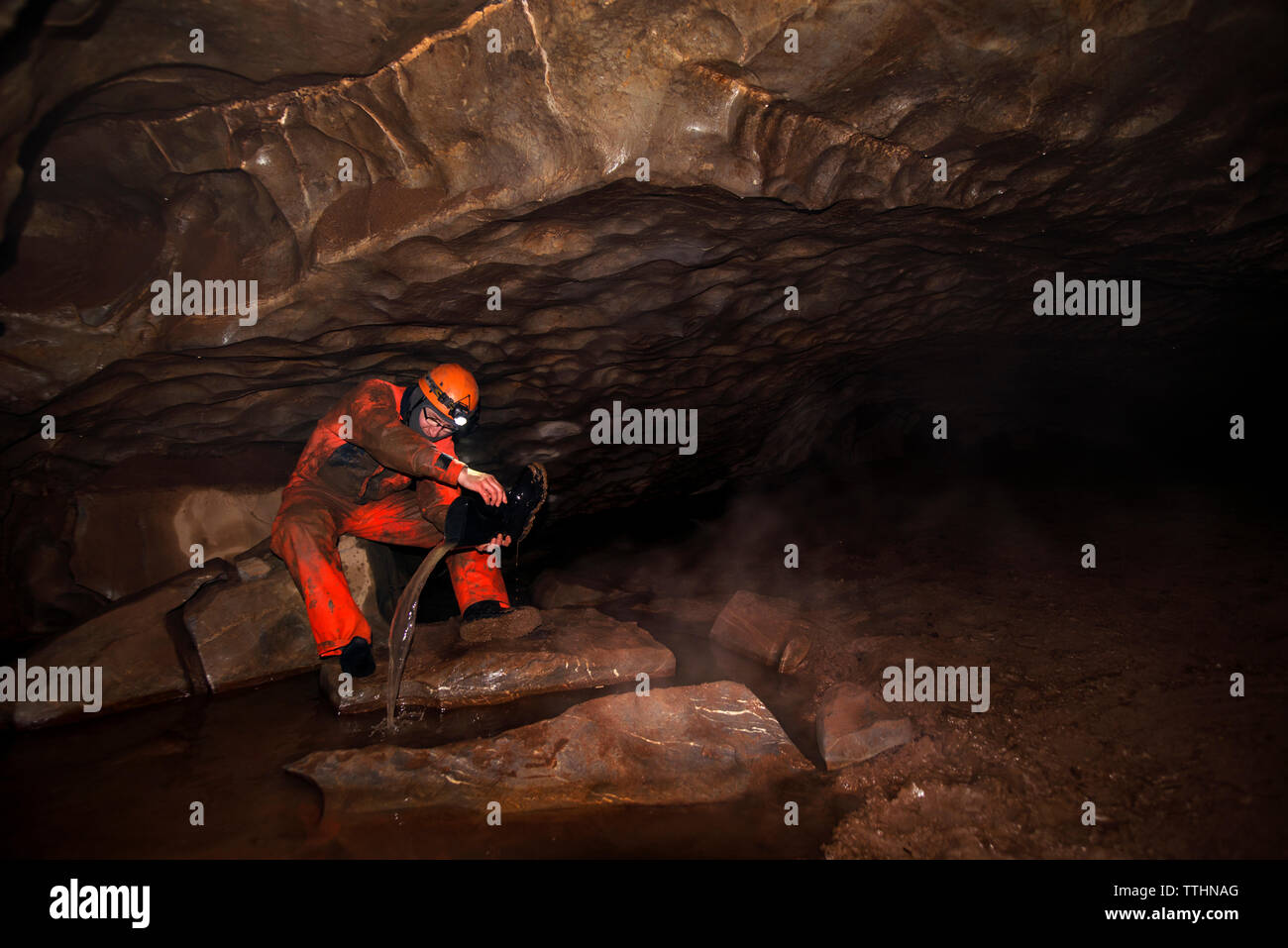 Manual worker removing water from boot while sitting in cave Stock Photo