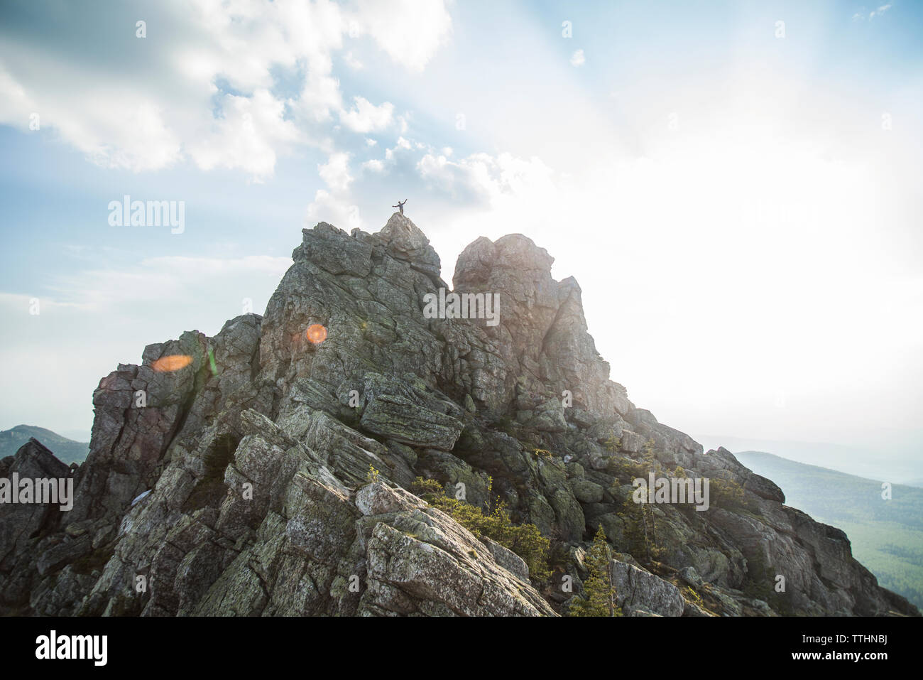 Distant view of hiker standing on mountain against cloudy sky Stock Photo