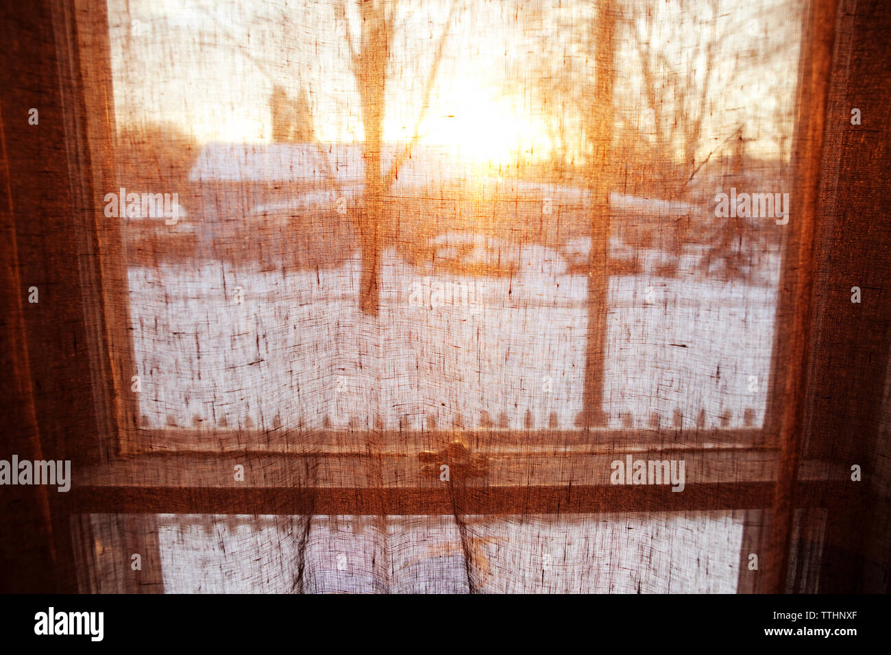 Snow covered field seen through curtain during sunset Stock Photo