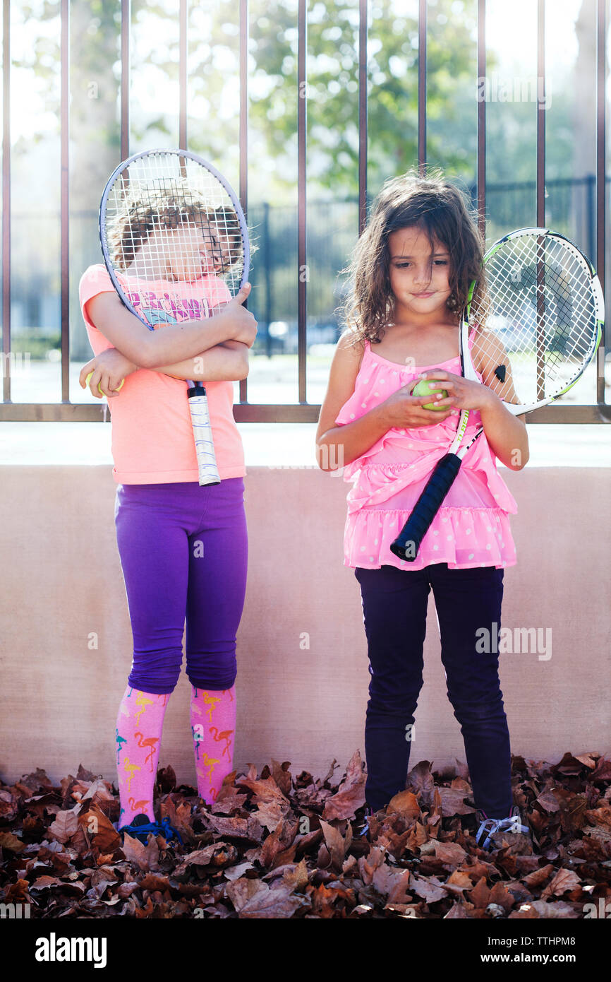 Children holding tennis racket and ball while standing against fence ...