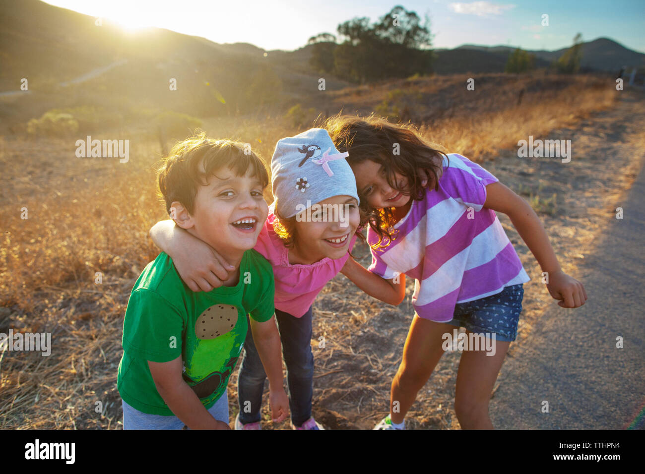 Portrait of boy with sister enjoying on road by field Stock Photo