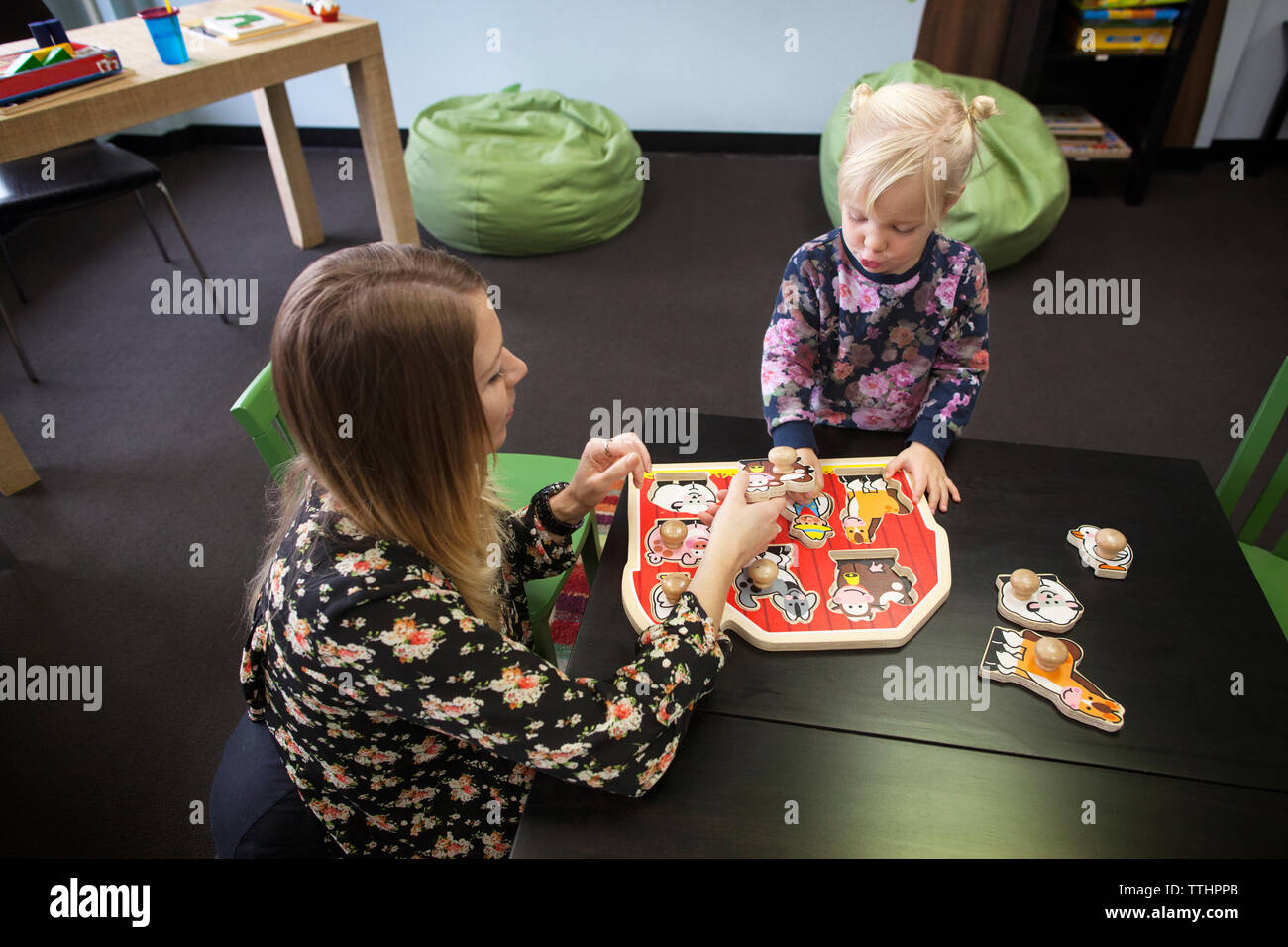 Teacher assisting girl to play knob puzzle at table in preschool Stock Photo