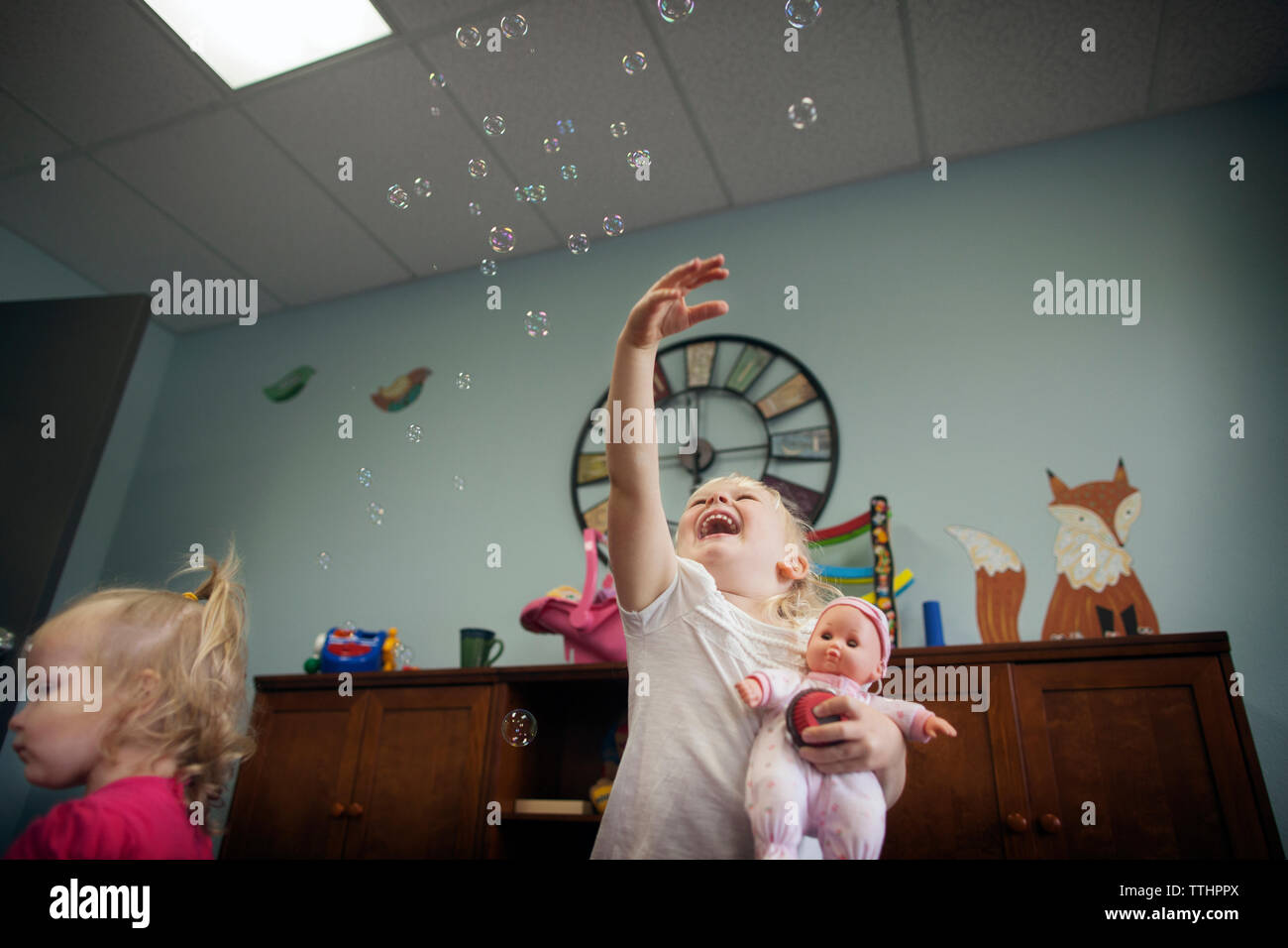 Low angle view of cheerful girl playing with bubbles at preschool Stock Photo
