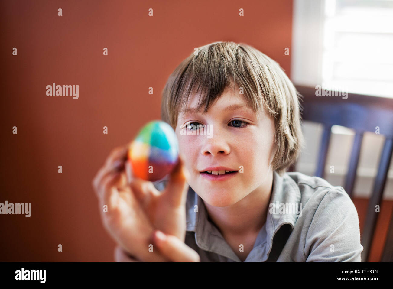 Boy looking at decorated easter egg while sitting on chair at home Stock Photo