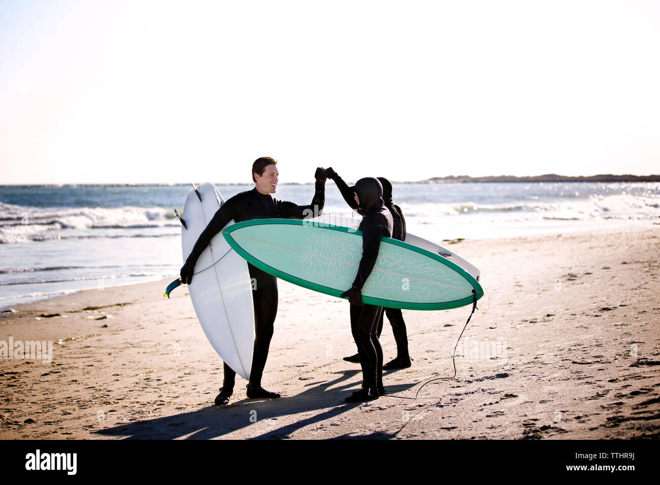 Surfers doing fist bump while standing at beach Stock Photo