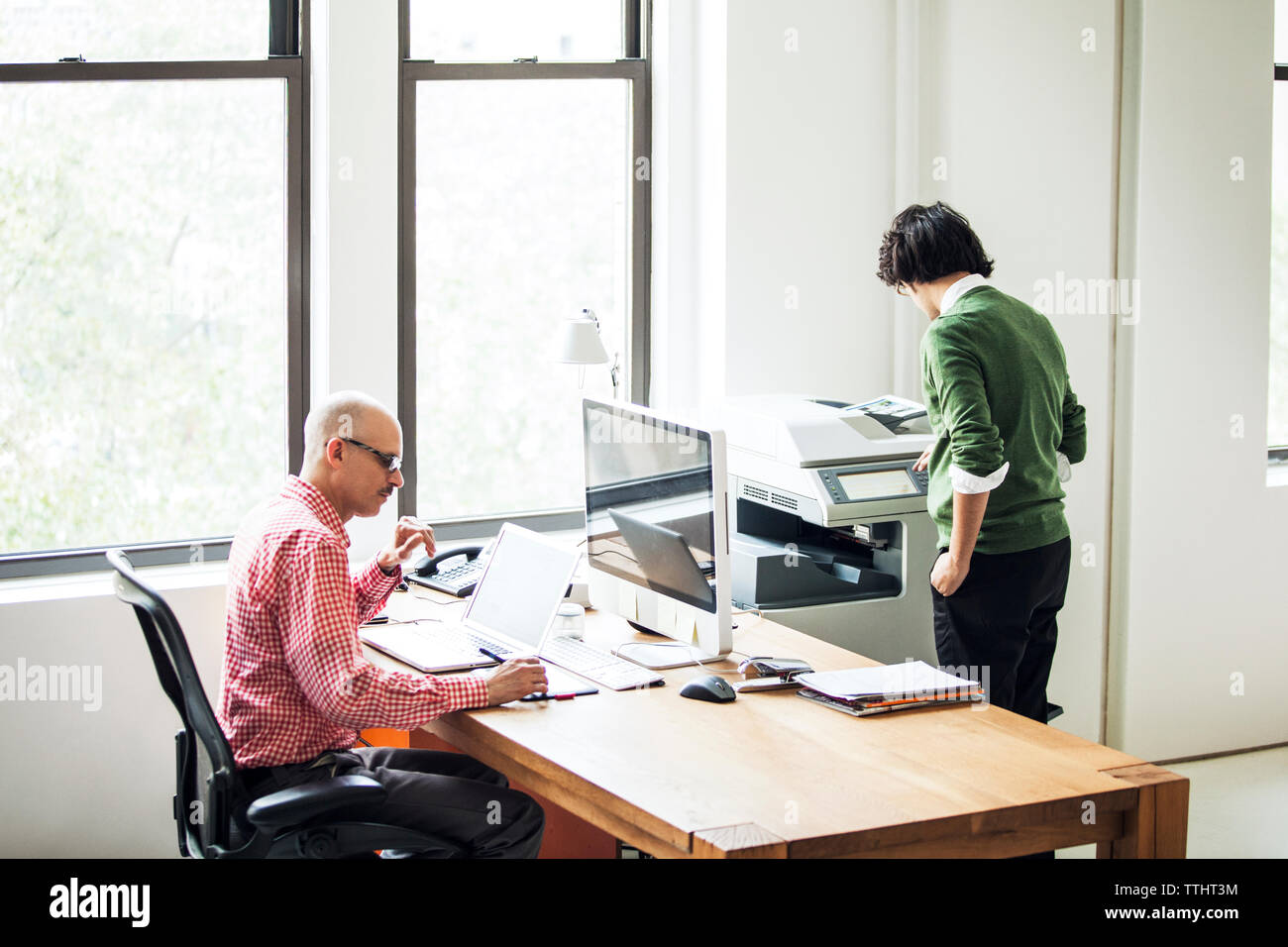 businessman working on computer while coworker using printer at office Stock Photo