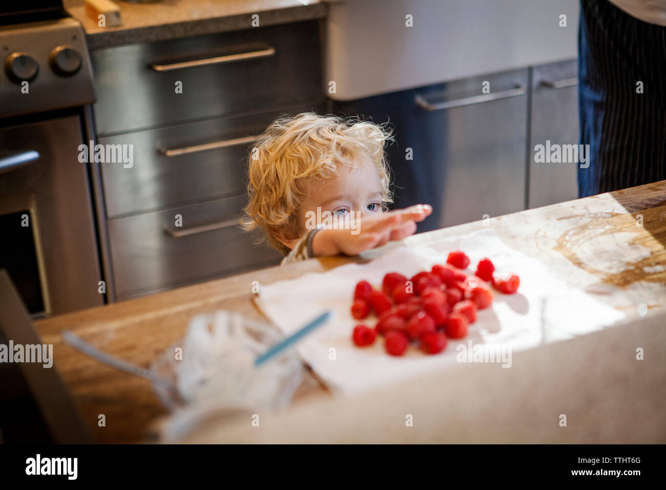 Cute boy looking at raspberries in kitchen Stock Photo