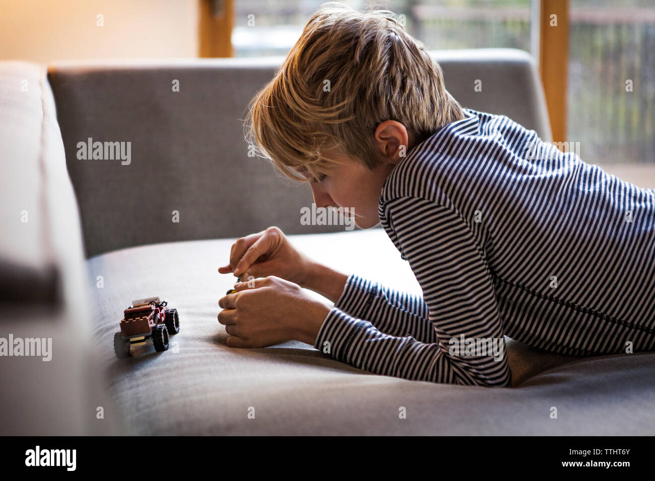 Boy playing with toys while lying on sofa at home Stock Photo