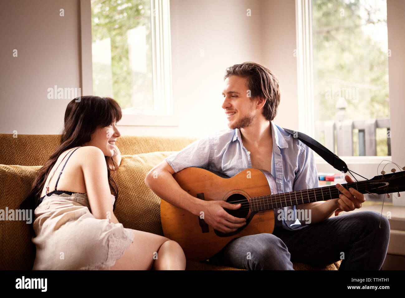 Man playing guitar while sitting with girlfriend on sofa at home Stock Photo