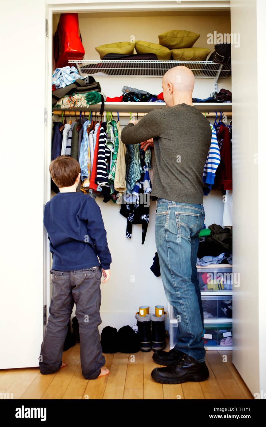 Boy standing with father removing clothes from wardrobe Stock Photo