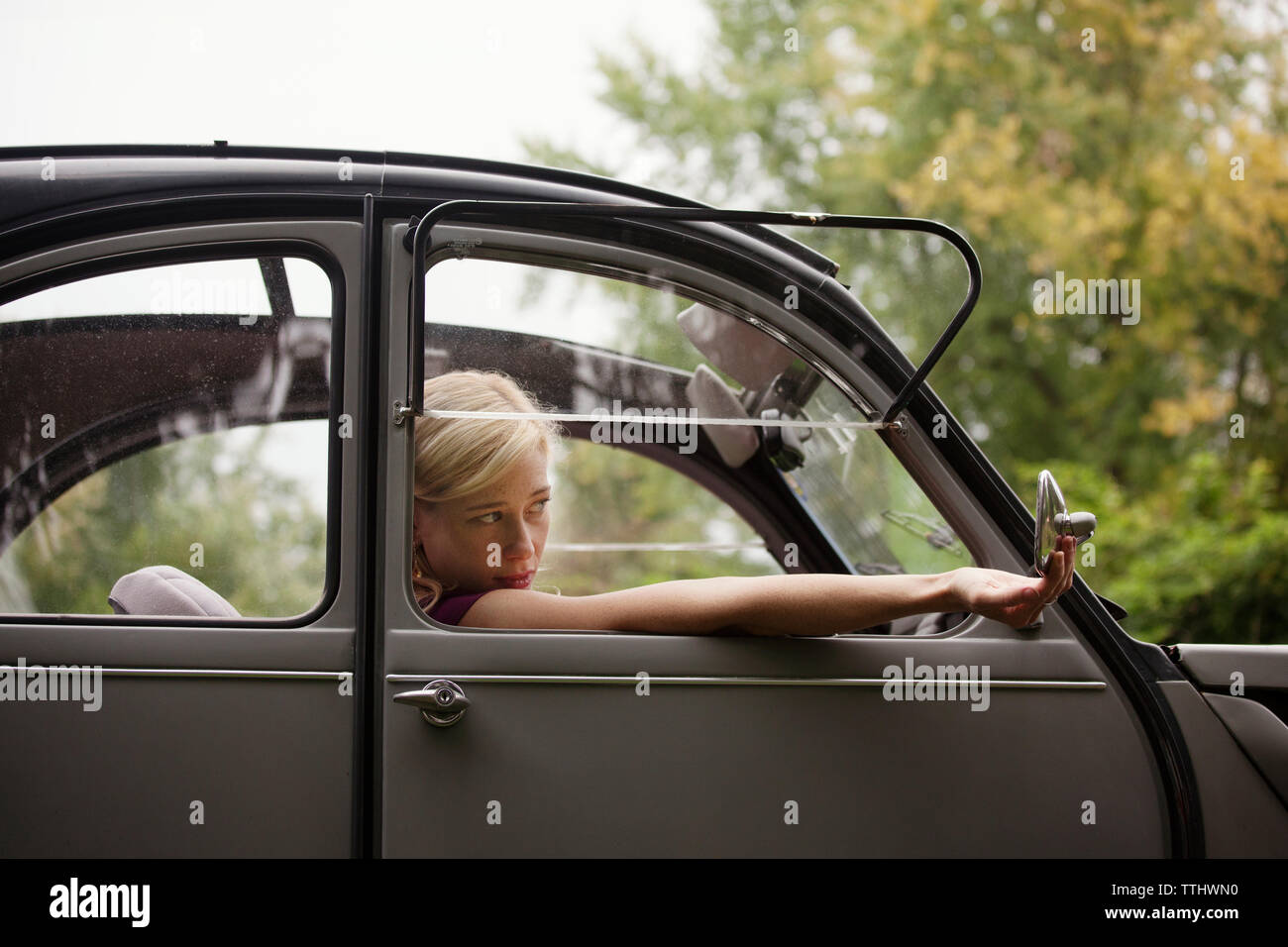 Woman looking at side-view mirror while sitting in vintage car Stock Photo