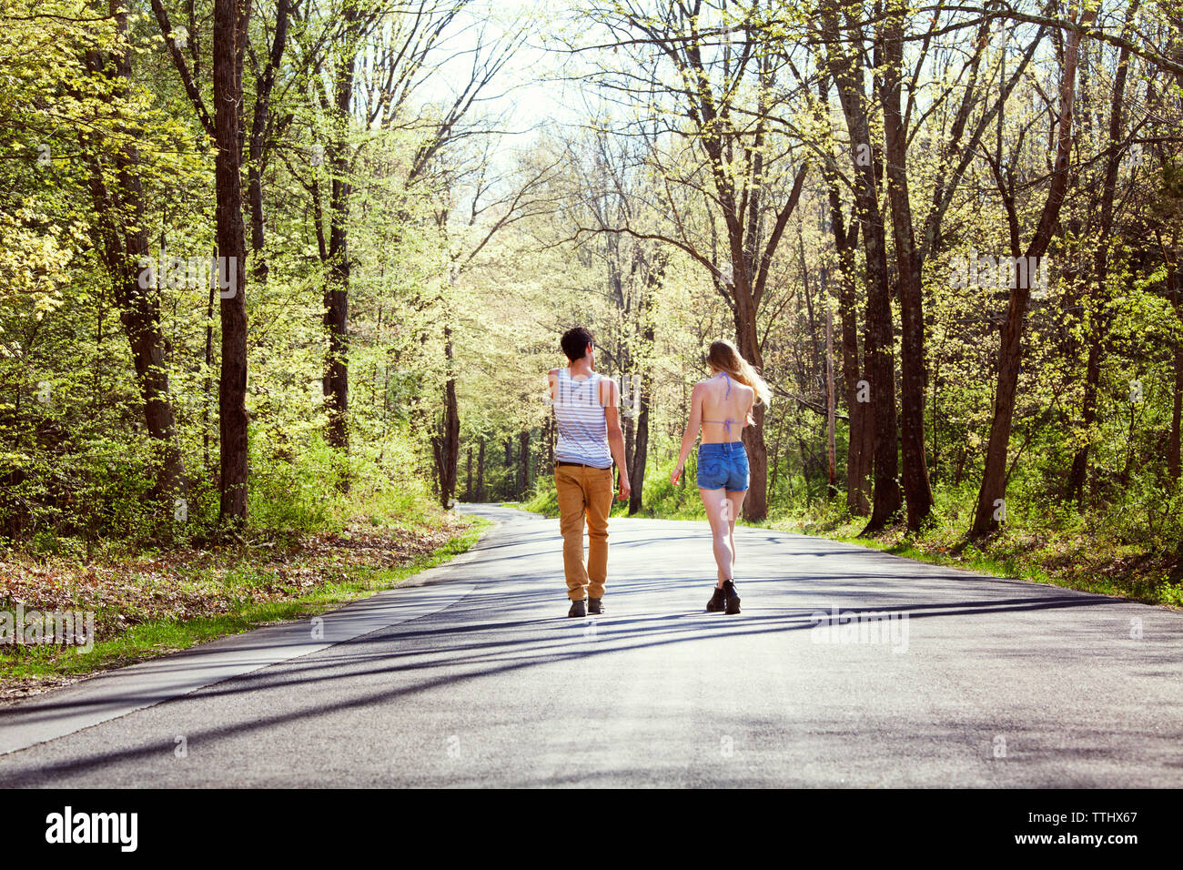 Rear view of couple walking on road amidst trees Stock Photo - Alamy