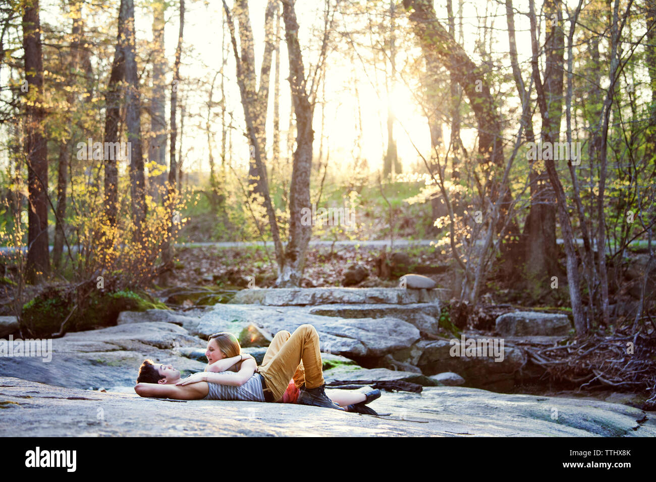 Happy couple talking while lying on rock at forest Stock Photo