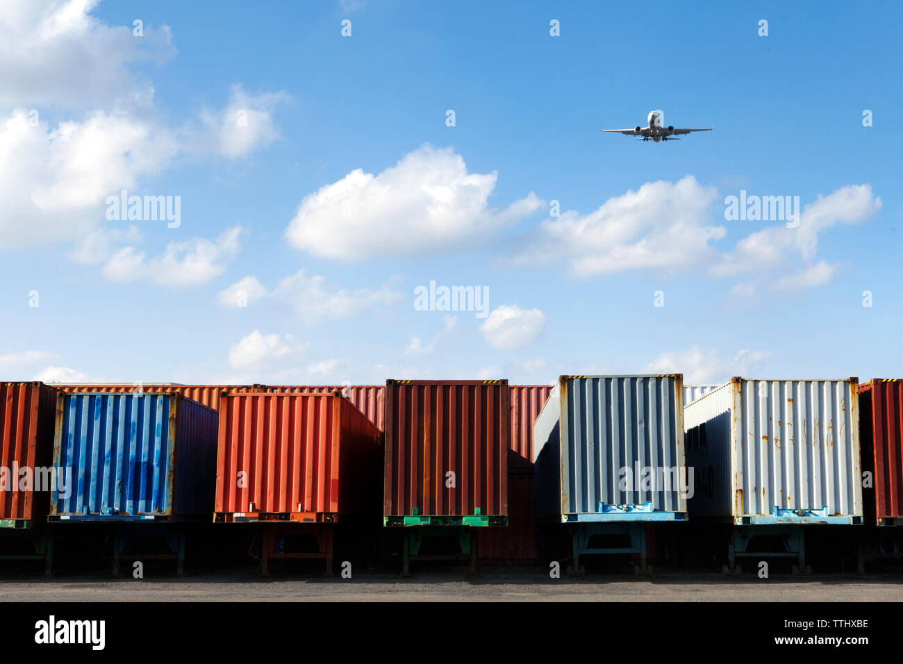 Airplane flying over cargo containers against sky Stock Photo