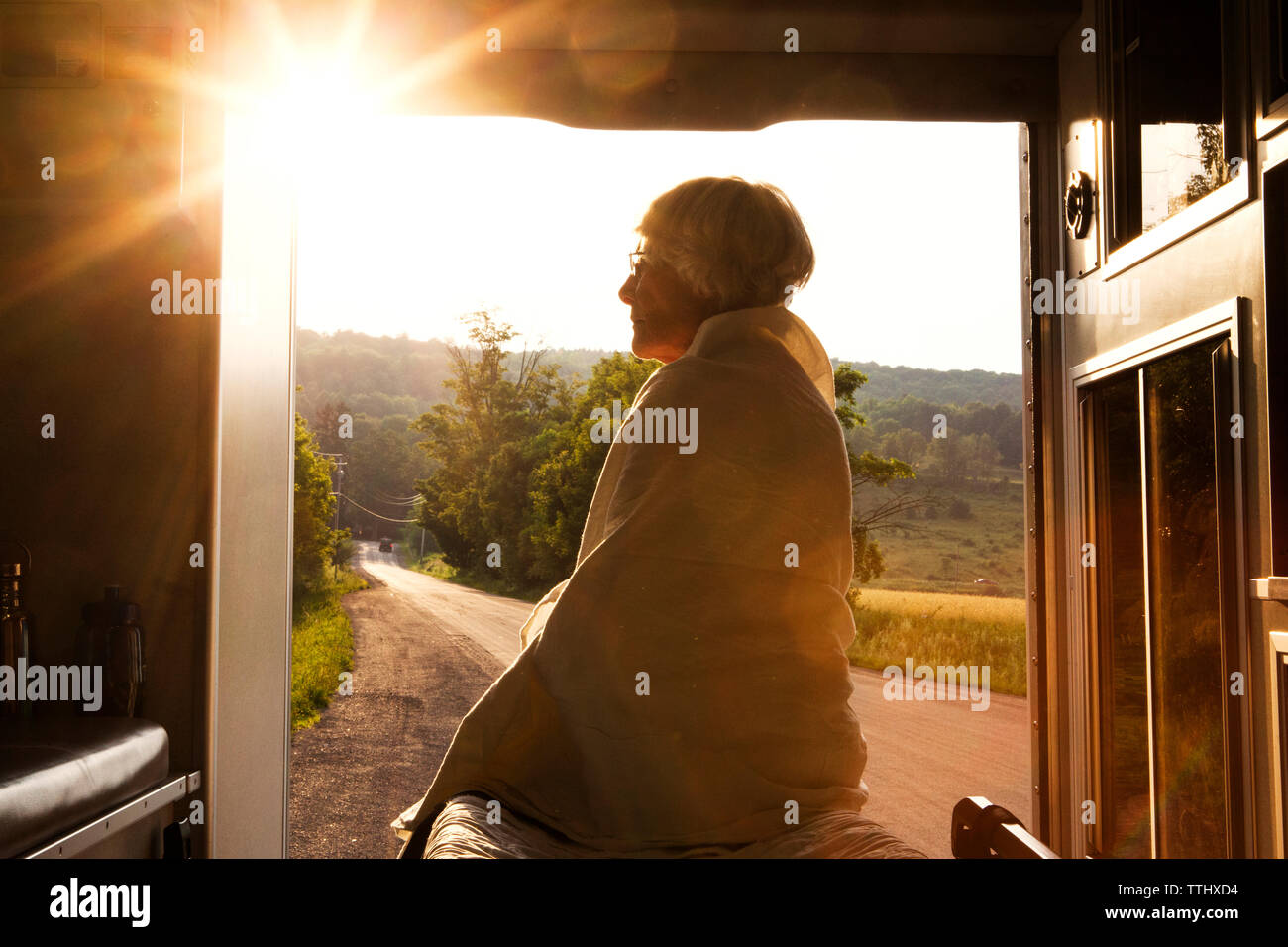 Woman wrapped in blanket sitting in ambulance during sunset Stock Photo