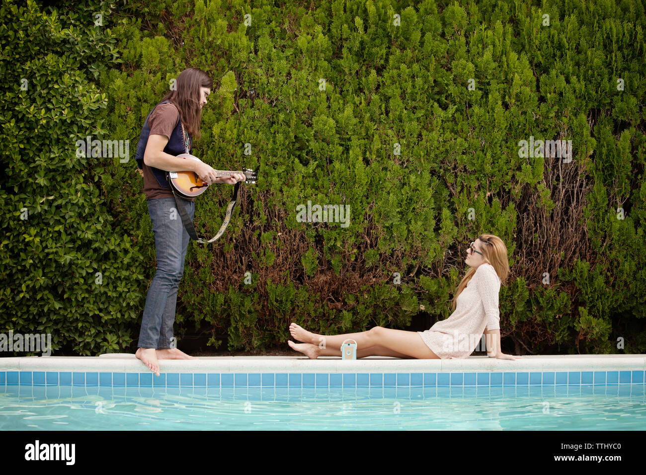 Man playing mandolin while woman sitting by swimming pool Stock Photo