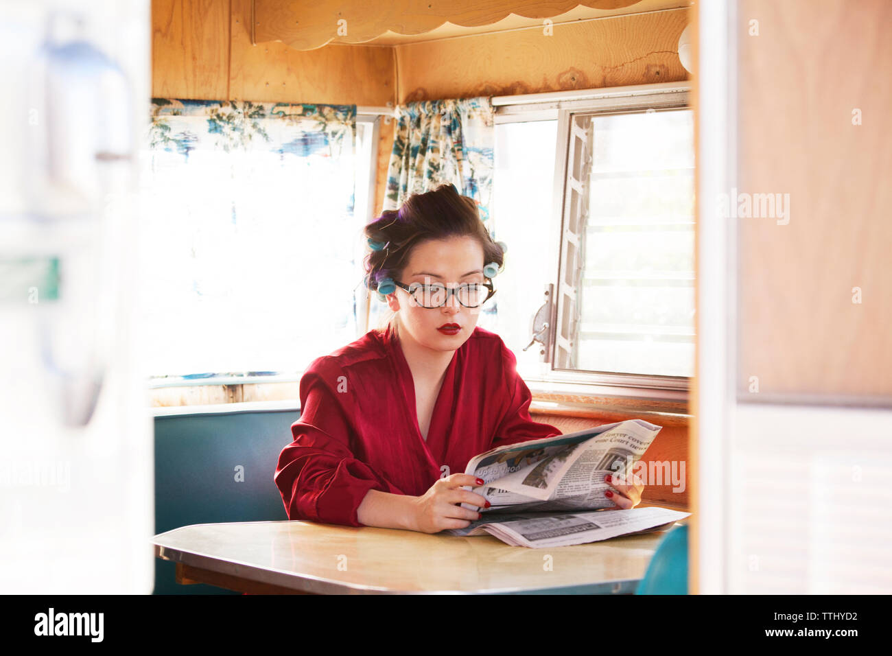 Woman reading newspaper while sitting by table in camper van Stock Photo