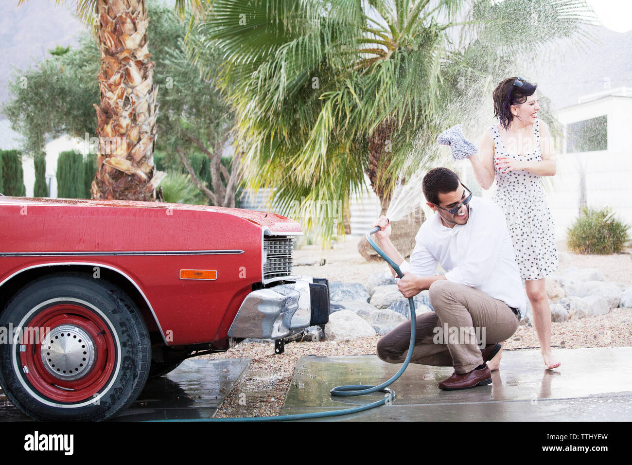 Man spraying water on woman while washing car at parking lot Stock Photo