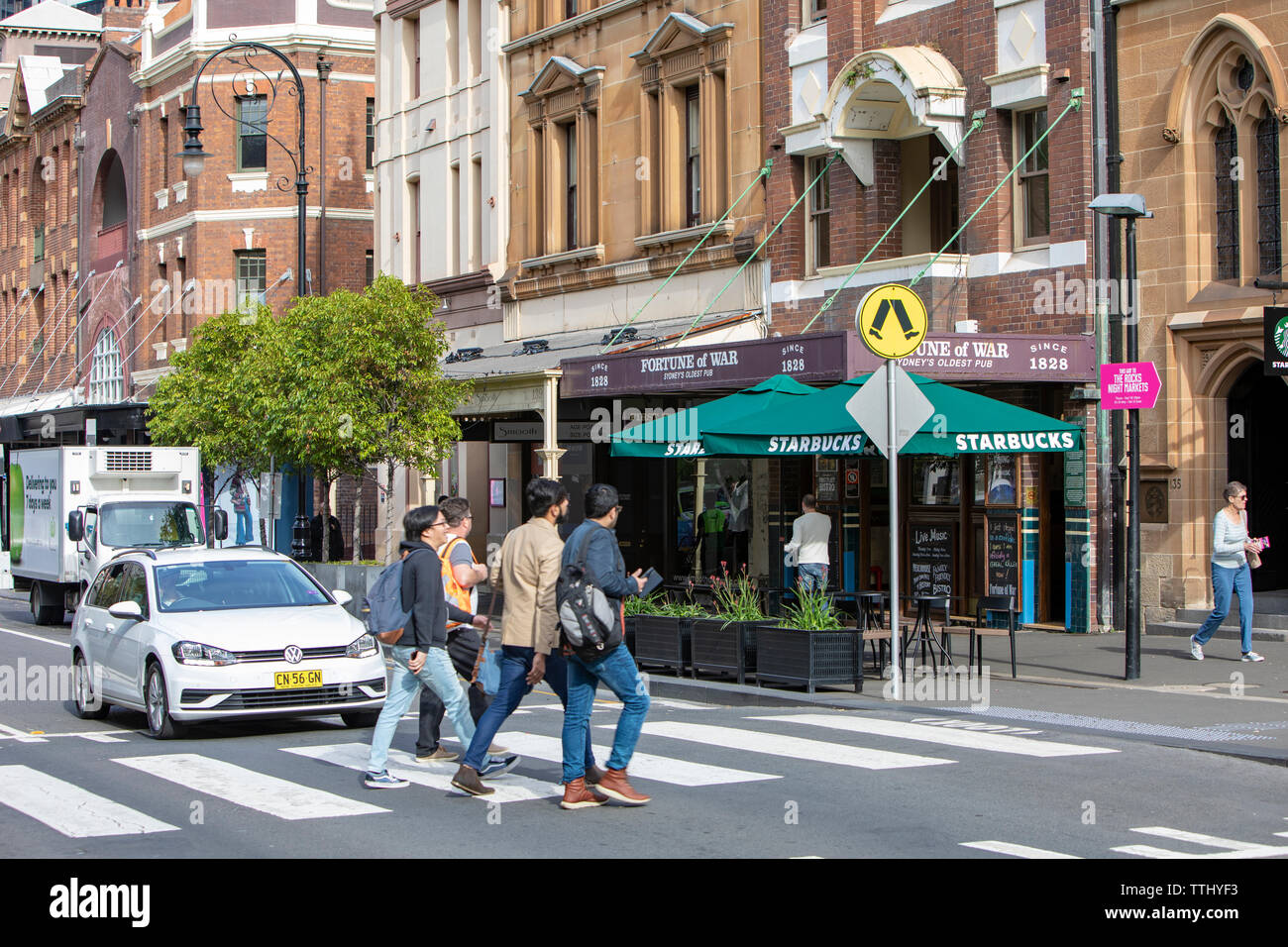 Men crossing the road in the Rocks area of Sydney beside Fortune of war sydney's oldest pub and starbucks cafe,Sydney,Australia Stock Photo