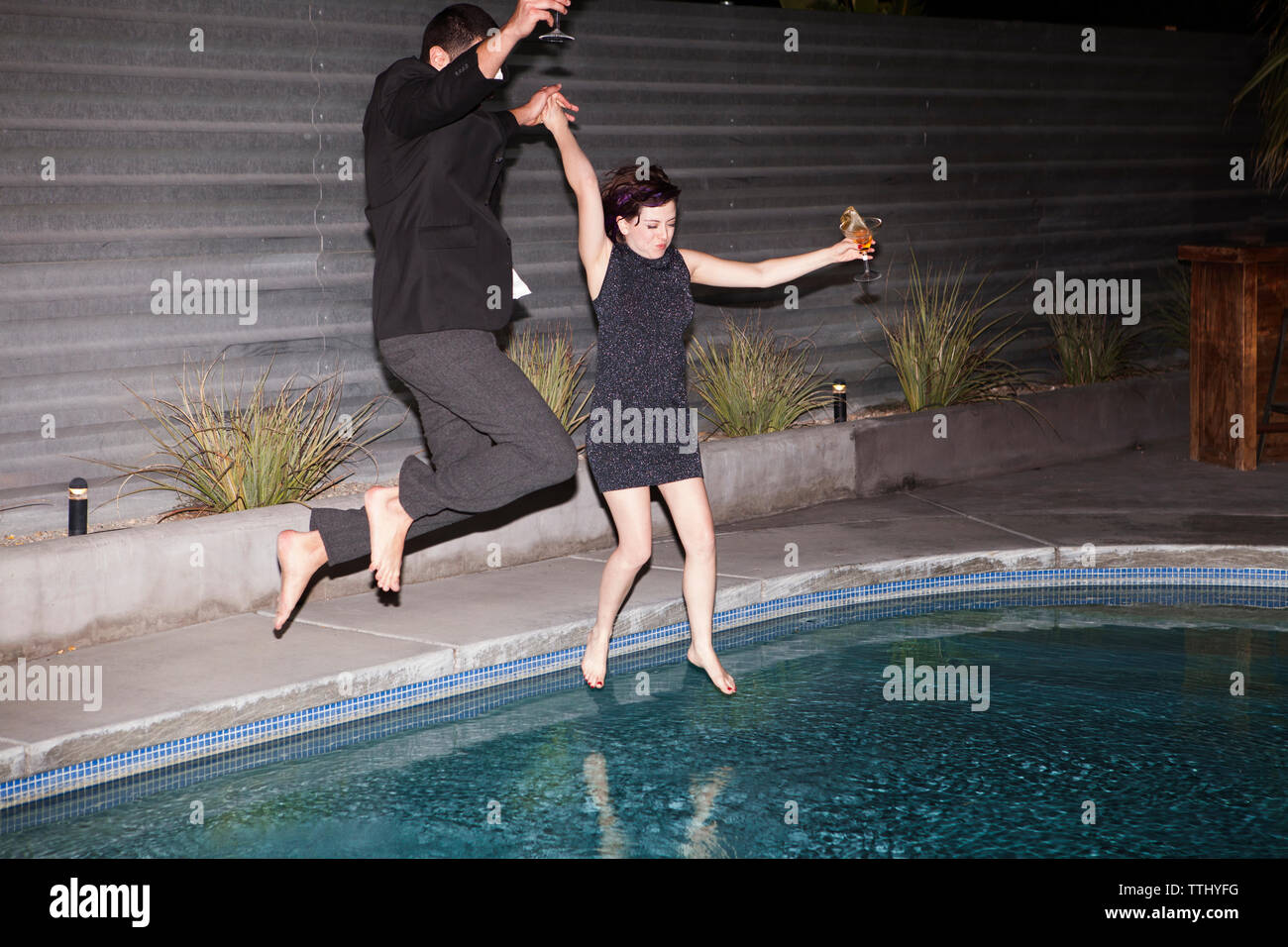Couple with holding hands jumping in swimming pool Stock Photo