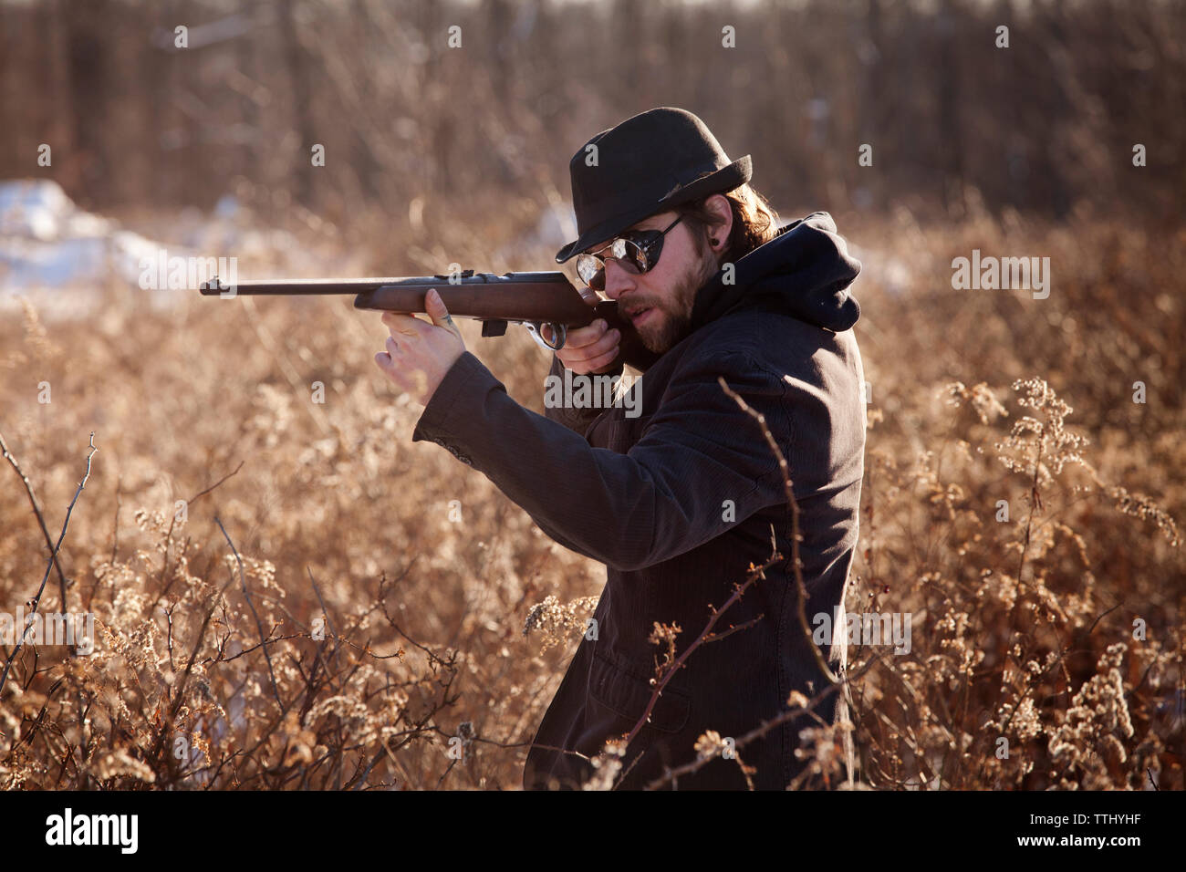 Man aiming with rifle while standing by plants Stock Photo