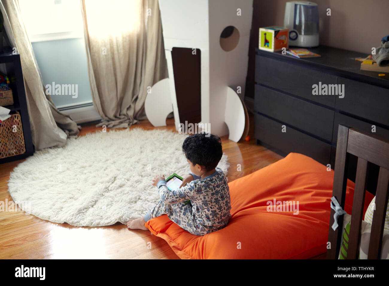 Rear view of boy using tablet while sitting on bean bag at home Stock ...