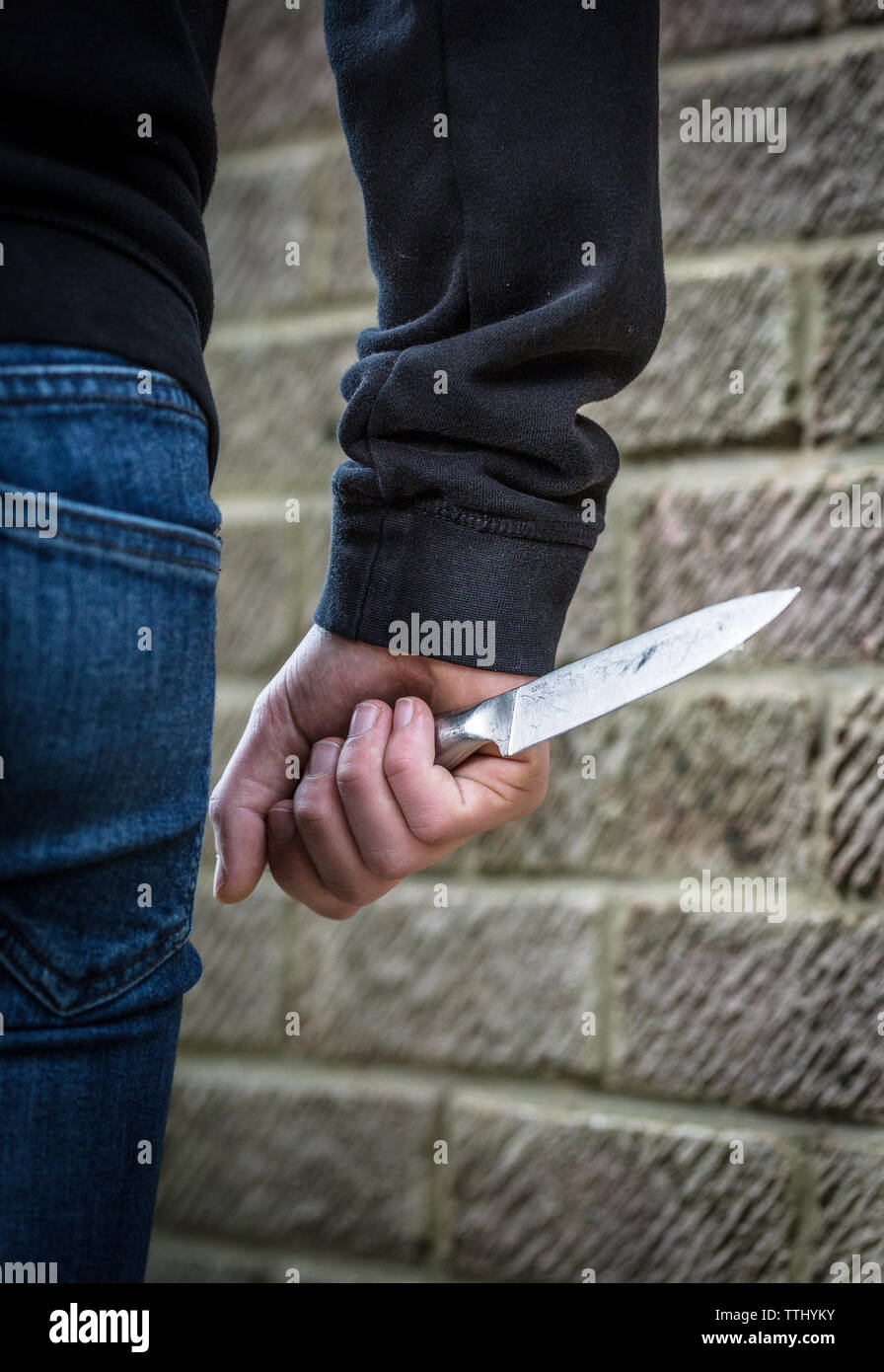 Knife Crime, Teenager in a hoody carrying a knife on the street in the UK Stock Photo