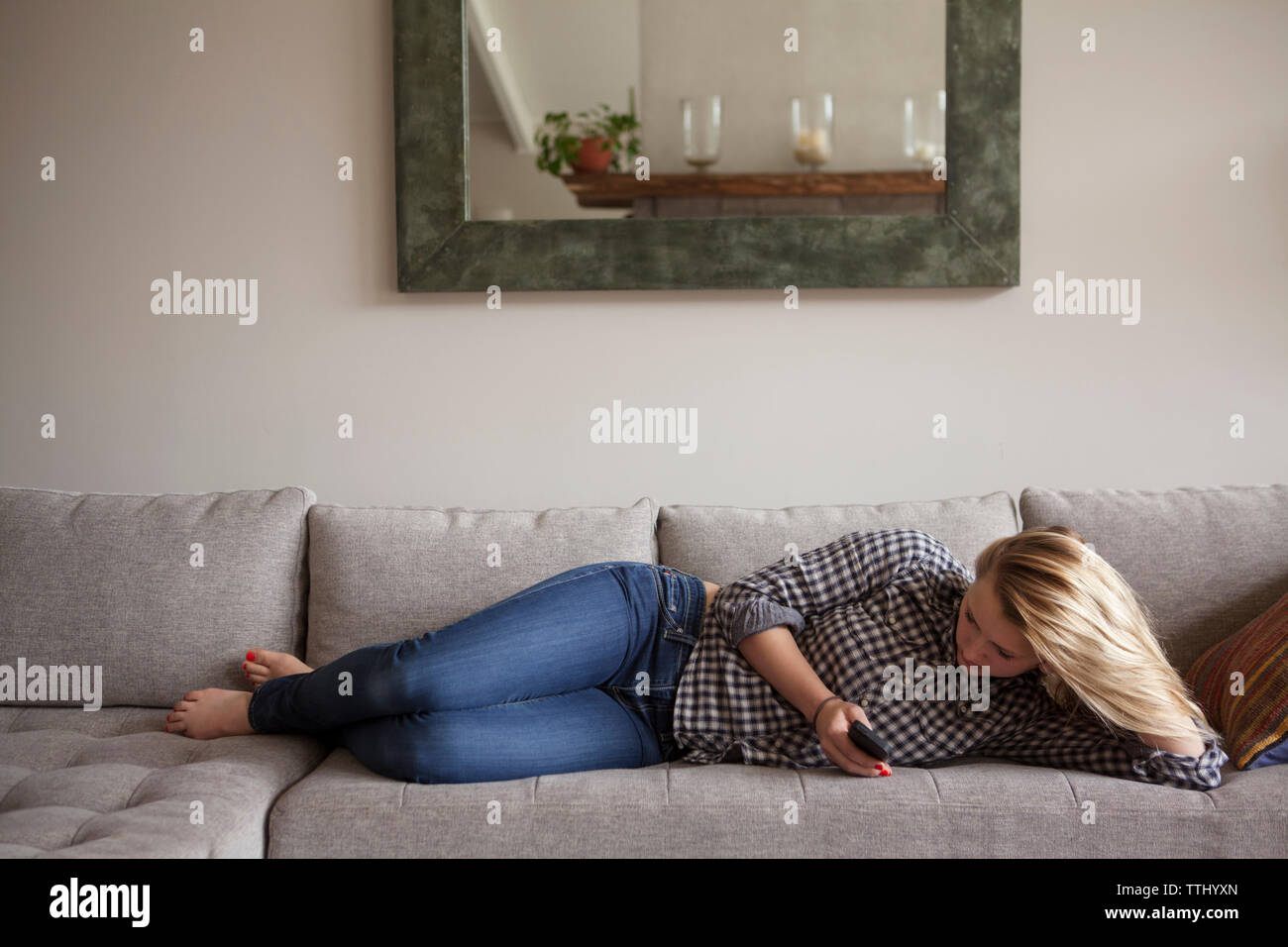Full length of girl using smart phone while lying on sofa at home Stock Photo