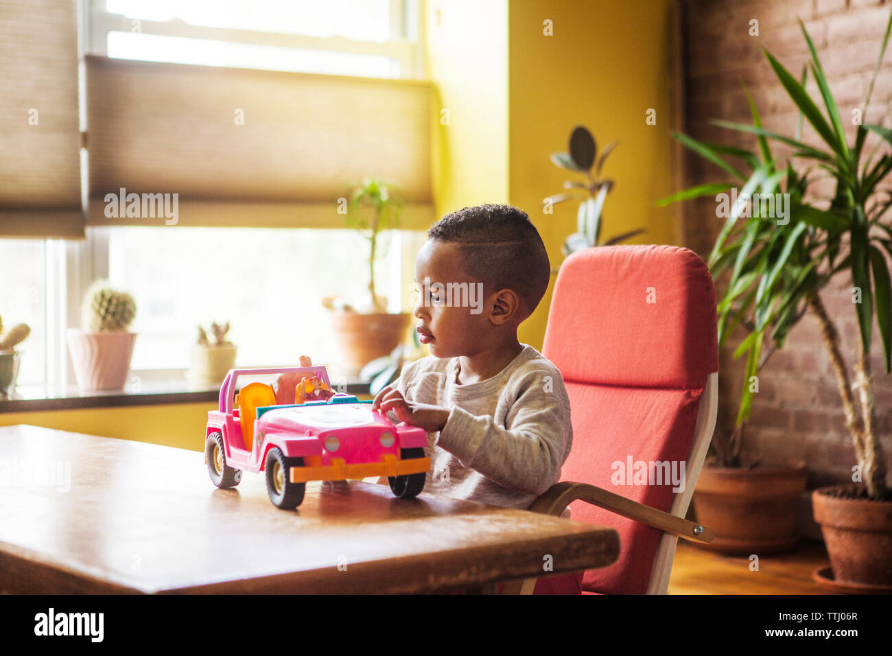 Boy playing with toy car while sitting on chair by table at home Stock ...