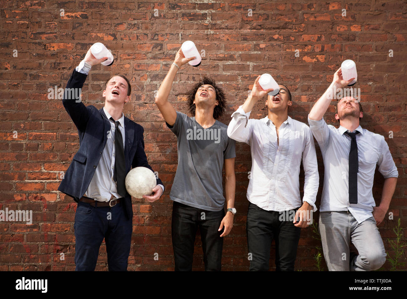 Friends drinking water while standing against brick wall Stock Photo