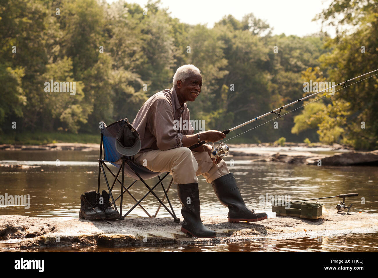 Happy man fishing while sitting by lake Stock Photo - Alamy
