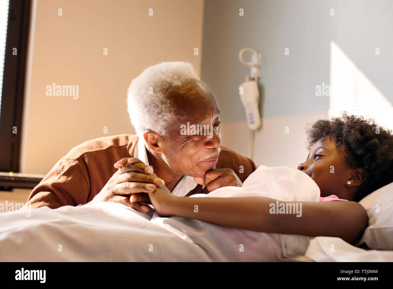 Grandfather looking at girl lying on bed in hospital Stock Photo