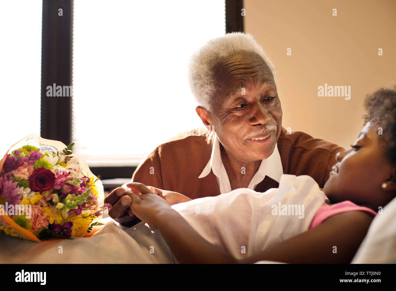 Grandfather sitting by girl on bed in hospital Stock Photo