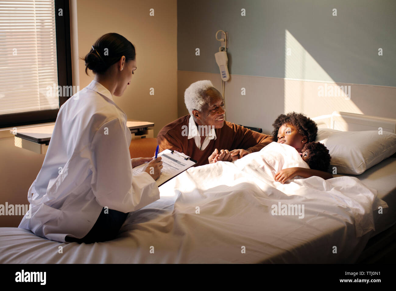 Doctor writing report while grandfather looking at girl in hospital Stock Photo