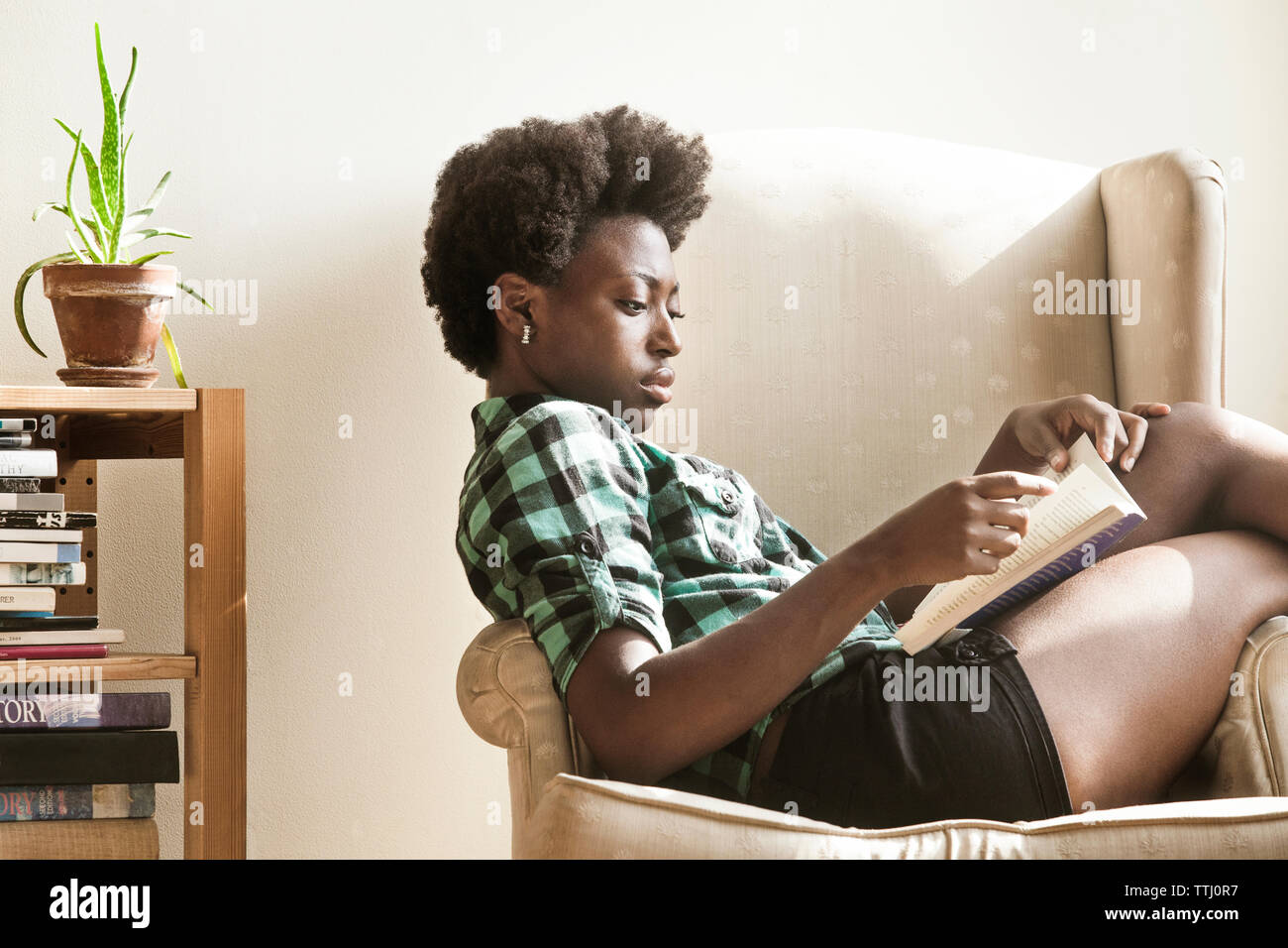 Woman reading book while sitting on armchair at home Stock Photo