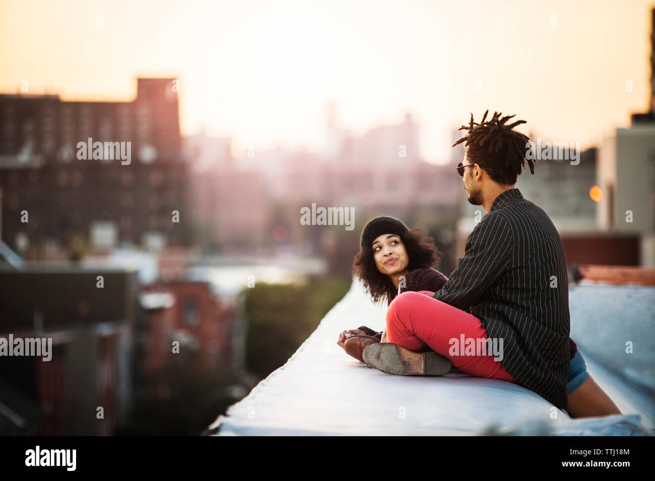 Woman looking at man sitting on retaining wall during sunset Stock Photo
