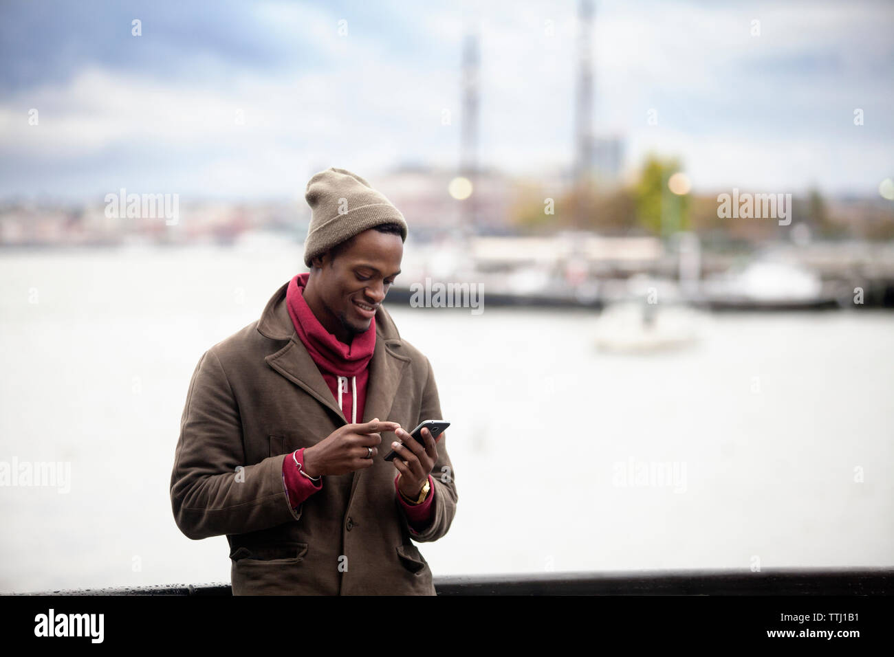 Smiling man using mobile phone while standing by railing against sea Stock Photo