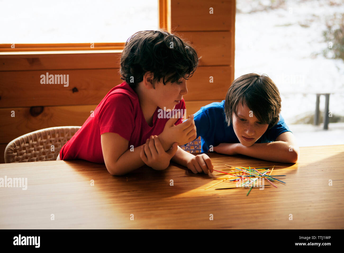 Siblings playing pick up sticks at table in home Stock Photo