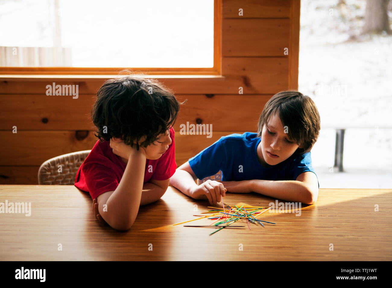Brothers playing pick up sticks at table in home Stock Photo