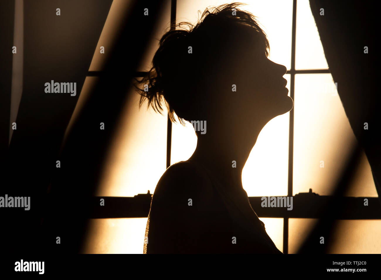 Silhouette woman standing against window at home Stock Photo