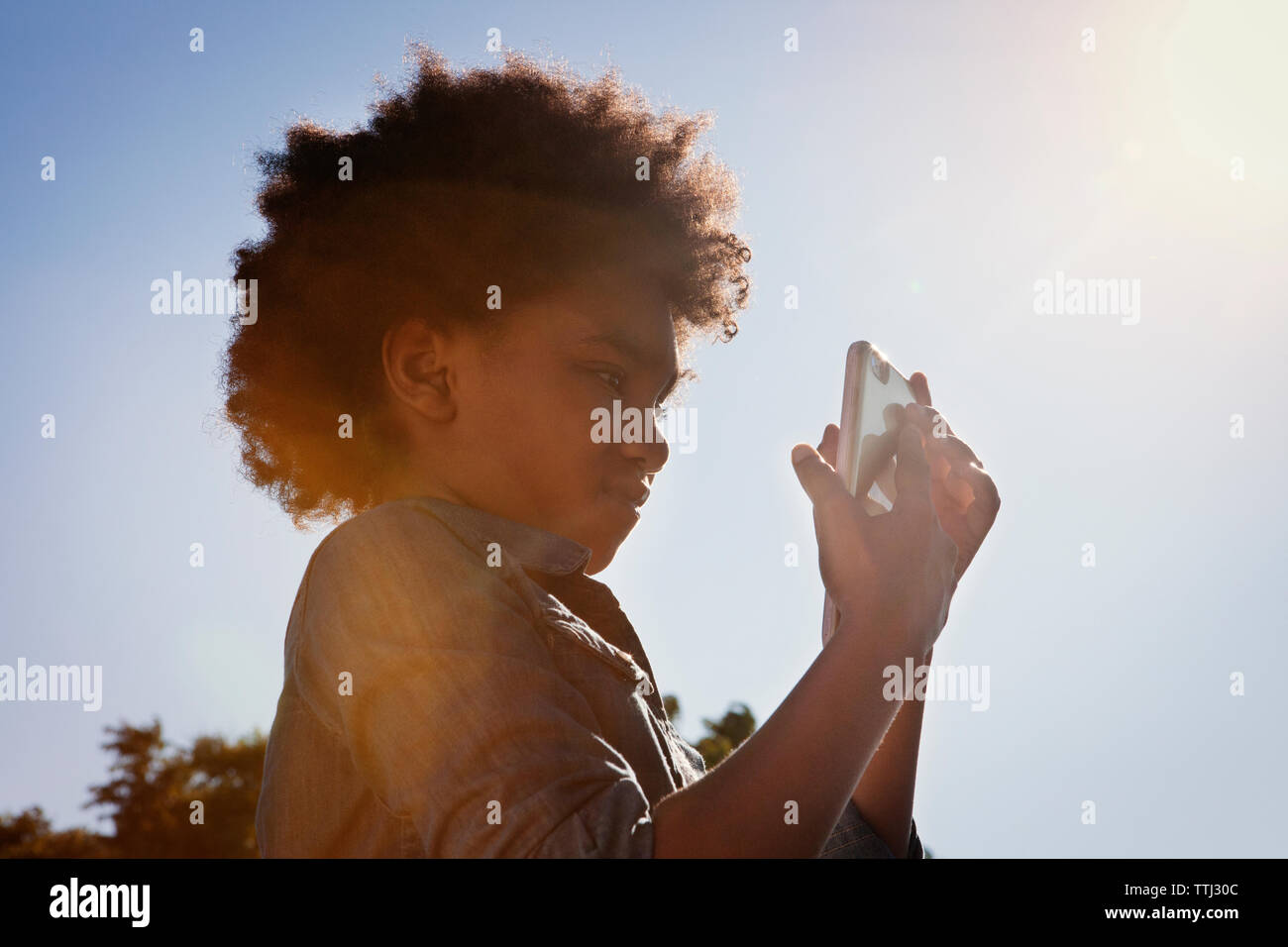 Low angle view of girl using mobile phone against clear sky Stock Photo