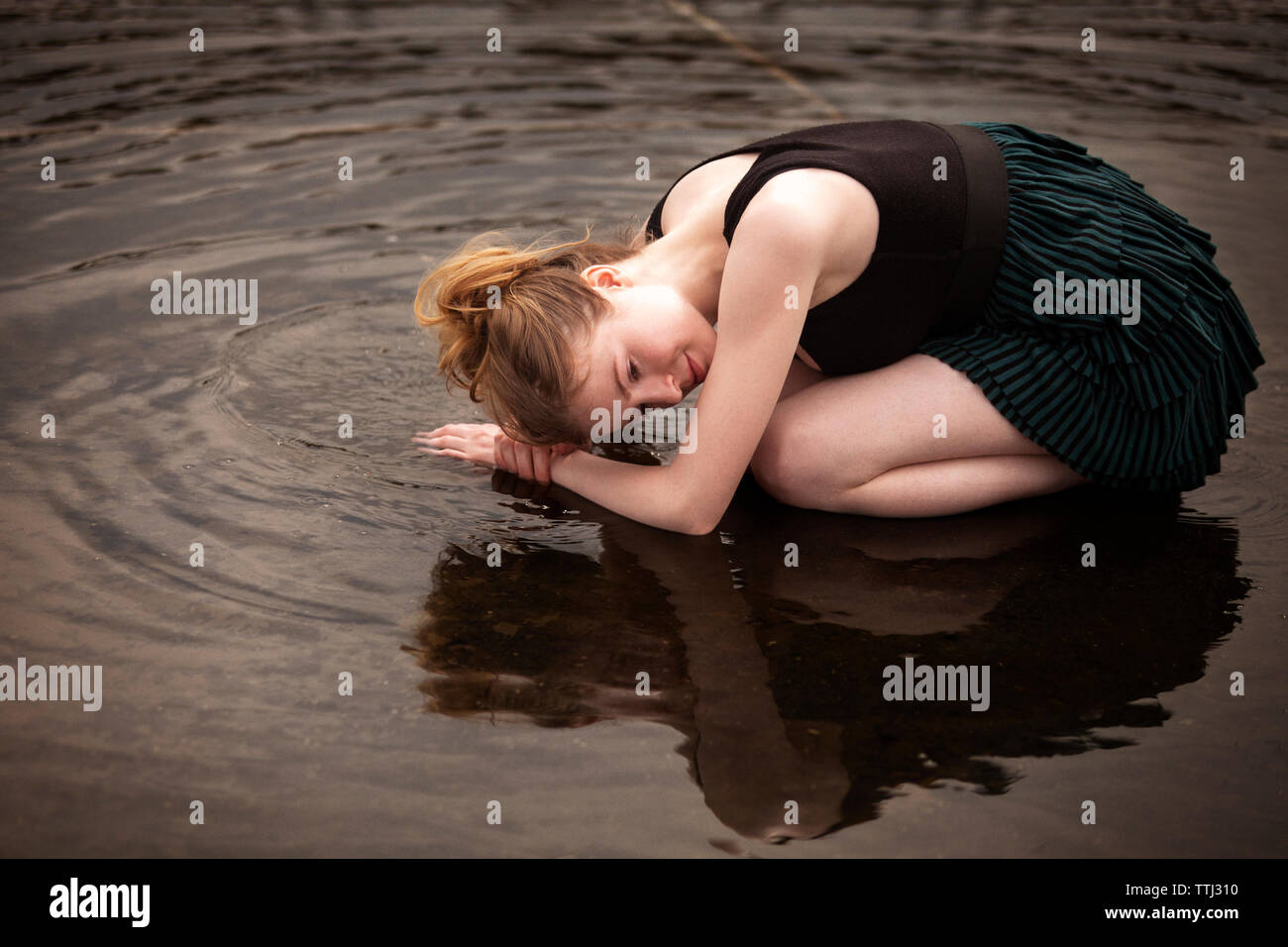 Side view of woman kneeling on shallow water at beach Stock Photo