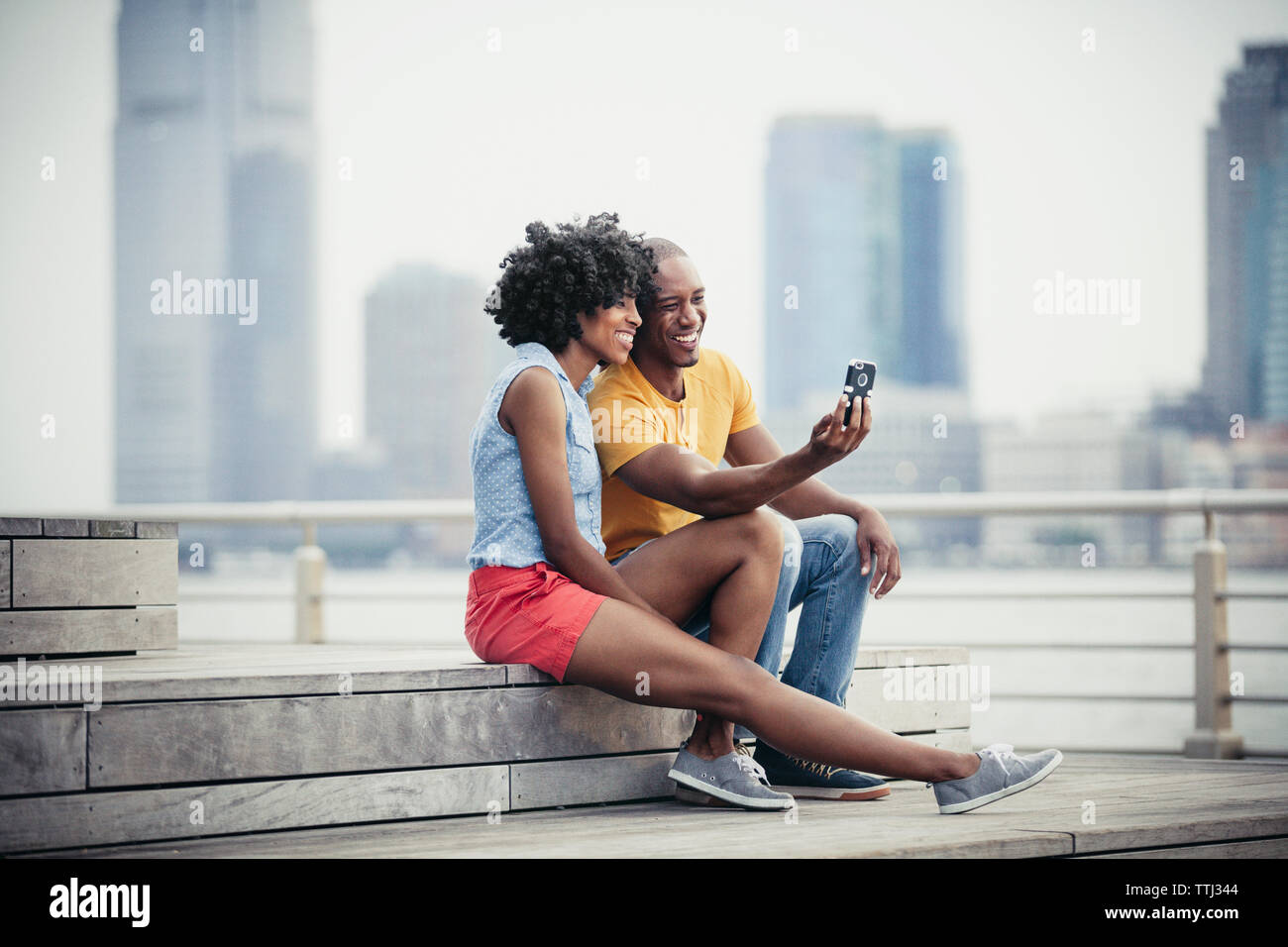 Smiling couple taking selfie while sitting on steps at promenade Stock Photo