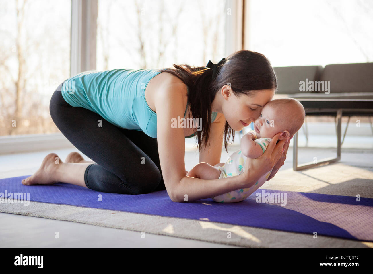 Loving mother holding baby girl while kneeling on exercise mat Stock Photo