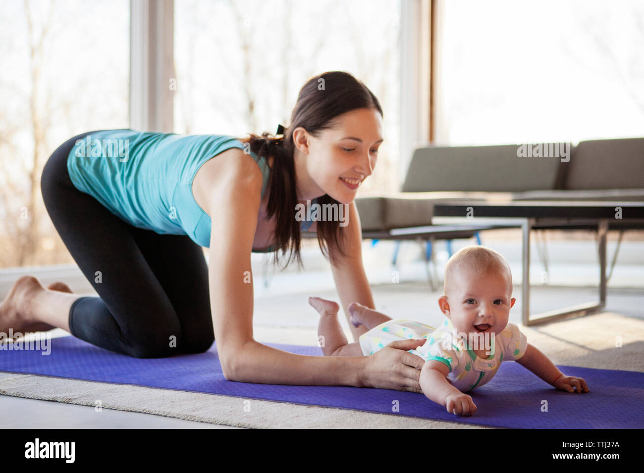 Happy mother holding baby girl while kneeling on exercise mat Stock Photo
