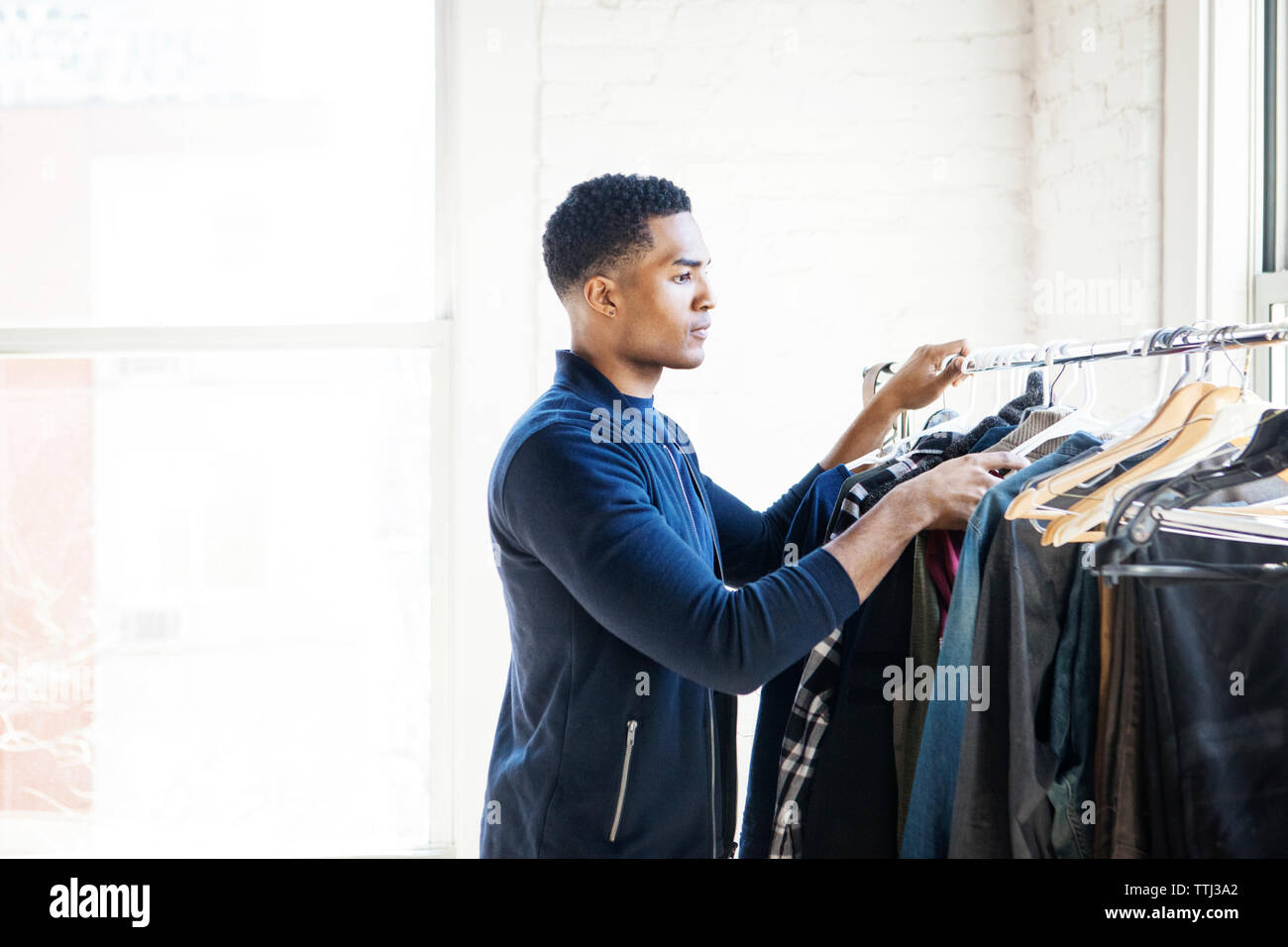 Side view of man choosing clothes from rack at home Stock Photo