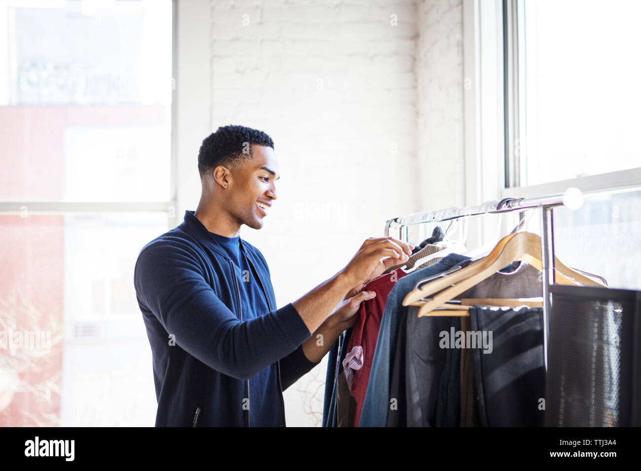 Side view of smiling man choosing clothes from rack at home Stock Photo